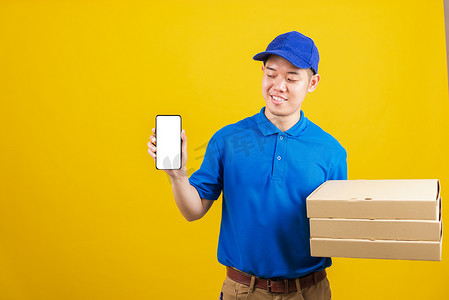 身穿蓝色制服微笑的送货服务男子拿着纸容器，用于外卖披萨盒包并展示智能手机