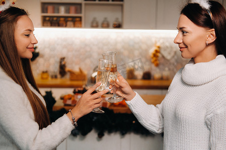 家庭环境摄影照片_圣诞节时，两个女孩在舒适的家庭环境中，手里拿着香槟。