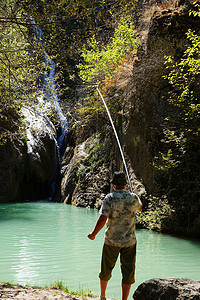男人在有瀑布的山湖里钓鱼，后视