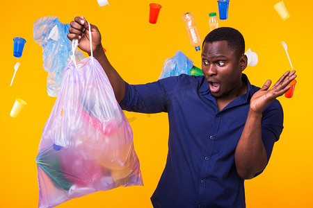 垃圾、塑料回收、污染和环境概念问题 — 黄色背景下携带垃圾袋的男子感到惊讶