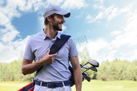 男性高尔夫球手在高尔夫俱乐部绿草旁行走时背着高尔夫球袋的肖像。