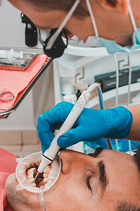 私人诊所摄影照片_牙科诊所，私人诊所，牙医使用双筒望远镜以获得最佳效果和工作，去除牙垢的过程。
