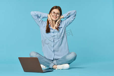 上学背景摄影照片_坐在地板上学习学生技术蓝色背景的笔记本电脑的妇女