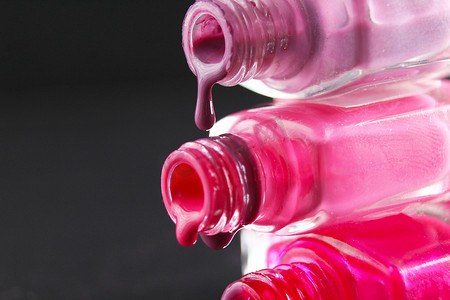 粉色指甲油摄影照片_黑色深色背景上，一滴红胡子粉色指甲油从瓶子里流出，有复制空间