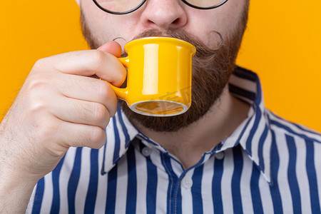 可爱的小杯子摄影照片_可爱自信的年轻人站在黄色背景下，用黄色小杯子喝咖啡的特写。