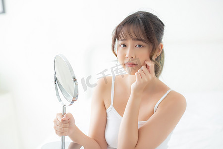 美丽的年轻亚洲女性看着镜子，脸上有痤疮问题