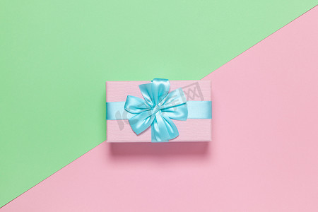 粉色礼盒，蓝色蝴蝶结，粉彩双色背景粉色和绿色，复制空间，平躺。 