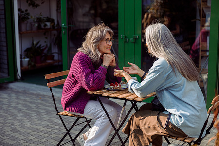 银发女人向坐在户外餐桌旁的成熟朋友讲故事