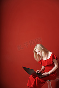 便携式椅子摄影照片_年轻的成年女性坐在椅子上，在笔记本电脑上工作