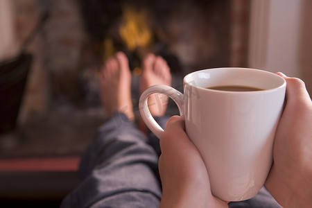 室内取暖摄影照片_手捧咖啡，在壁炉旁取暖