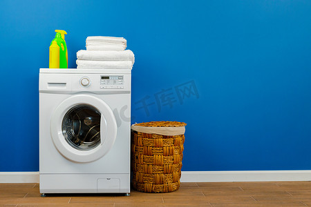 衣物收纳箱摄影照片_有衣物的洗衣机在蓝色墙壁背景