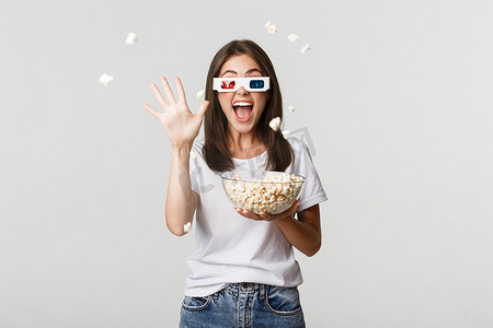 戴着 3D 眼镜的快乐迷人的年轻女孩，一边看电影一边向屏幕扔爆米花
