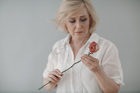 白衣先人摄影照片_身穿白衣、心烦意乱的老妇人一朵干枯的老玫瑰花枯萎了。