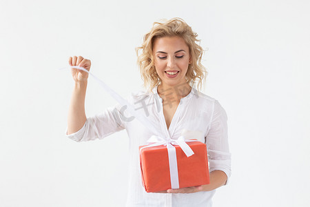 开朗漂亮的年轻金发女子手里拿着一个红色礼品盒，但背景是白色的。