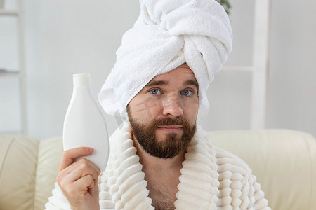 保湿器摄影照片_留着胡子的帅哥从容器中涂抹保湿身体霜。