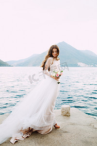 新娘手捧玫瑰花，站在科托尔湾的码头上