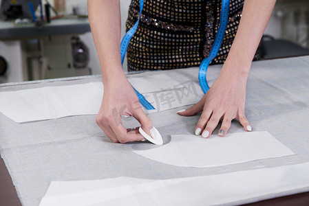 服装画线摄影照片_裁缝在工作，在工作室里用粉笔在布料上画线
