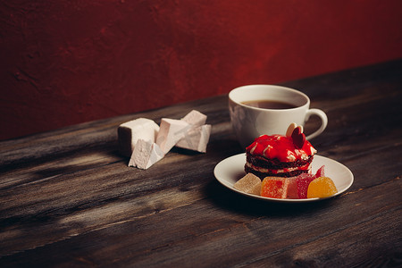 红色碟子摄影照片_一杯茶红色蛋糕在碟子糖果甜点木质背景上