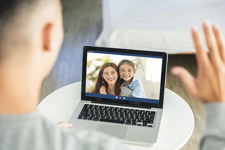 年轻人与妻子和可爱的女儿远程交谈，使用笔记本电脑在家中与家人在线交谈。