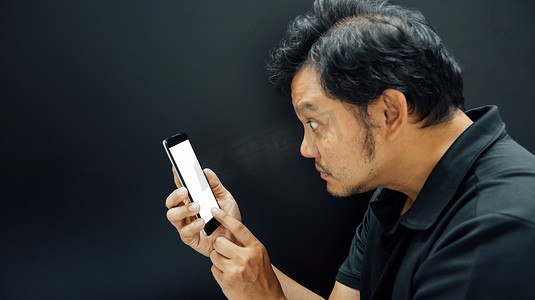 大吃一惊摄影照片_亚洲男人用深色智能手机惊呆了