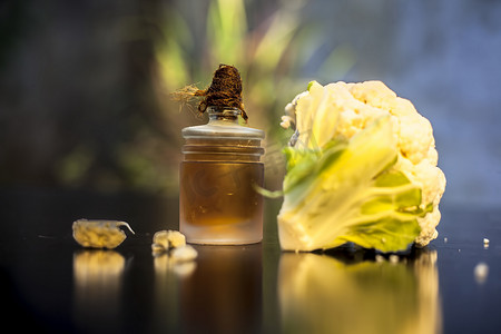 在黑色表面的一个小玻璃瓶中特写生花椰菜及其精油，有选择性的聚焦、创意照明和模糊的背景。