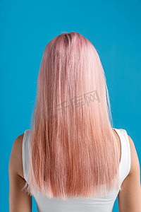 中时尚摄影照片_蓝色工作室背景中孤立的年轻女子美丽光滑的天然长粉色染发