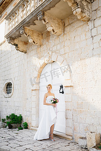一位身着优雅礼服、手里拿着花束的新娘站在佩拉斯特一栋美丽老建筑的白色门前