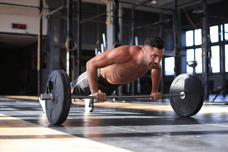健康、肌肉发达的男人在健身房里用杠铃做水平俯卧撑。