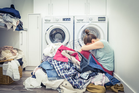 洗衣房洗衣机附近有一堆衣服、蓝色色调的压力大的女人
