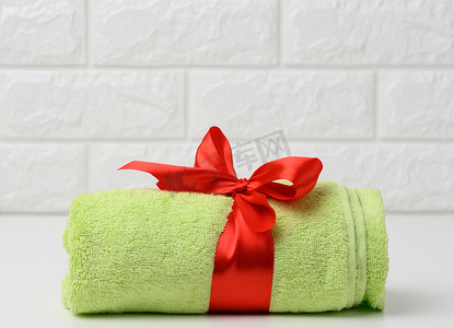 浴室白色架子上卷起的绿色毛巾，系着红色丝带