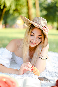 戴着帽子的年轻白人女孩穿着格子布躺在公园里，用智能手机冲浪。