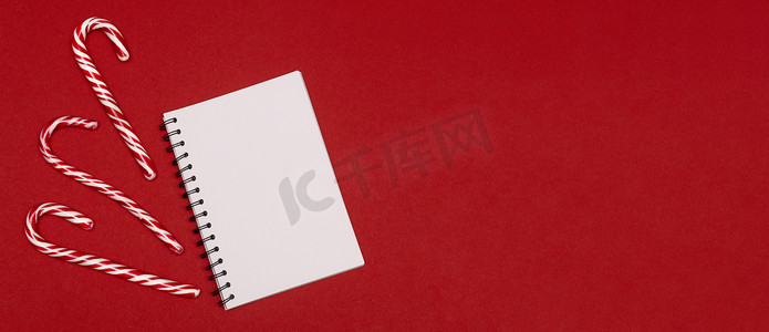 红色背景下白色笔记本和圣诞糖果的平铺