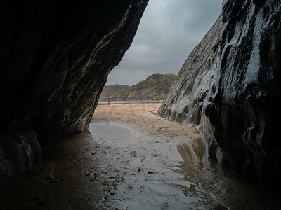 在阴天和潮湿的日子里，一个小洞穴俯瞰着英国威尔士高尔的卡斯韦尔湾海滩。