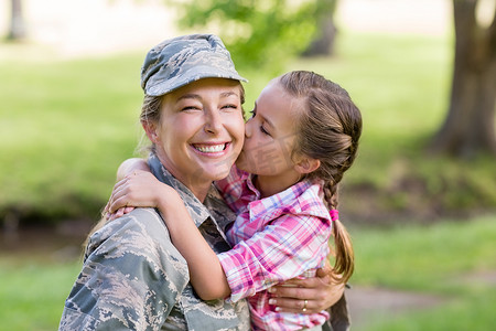 抱着花的女兵摄影照片_快乐的女兵在公园里被女儿亲吻