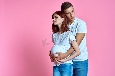 粉红色背景中的怀孕妈妈和快乐的父亲 等待婴儿的年轻家庭