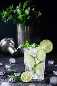 鸡尾酒莫吉托或柠檬水与石灰、 薄荷和冰在深色背景上。