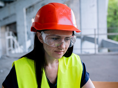个人电脑安全摄影照片_戴着防护头盔和护目镜的女建筑师在建筑工地新项目的个人电脑上工作