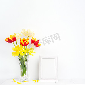 玻璃花瓶中的郁金香花，配有相框，放在白色木桌背景上，靠在家里干净的墙壁上，特写，母亲节装饰概念。