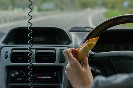 特写镜头，女性手在高速公路上行驶的汽车车轮后面拿着一个小圆面包