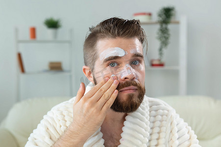 留胡子的家伙在镜子前涂抹面霜 皮肤护理和水疗中心的男士概念。