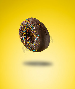 黄色背景上悬浮着彩色巧克力甜甜圈