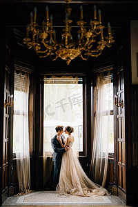 在老别墅大窗户的背景下，新郎差点亲吻新娘。