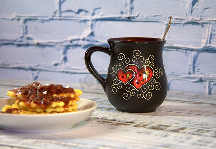 一个深色陶瓷杯，上面放着茶和一堆华夫饼，碟子上放着草莓酱。