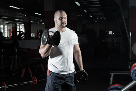 男性健美运动员在健身房里用哑铃进行锻炼