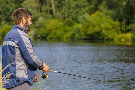 一个留着胡子的男人正在河边钓鱼。