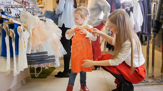 可爱的小女孩和妈妈在童装店买红色连衣裙