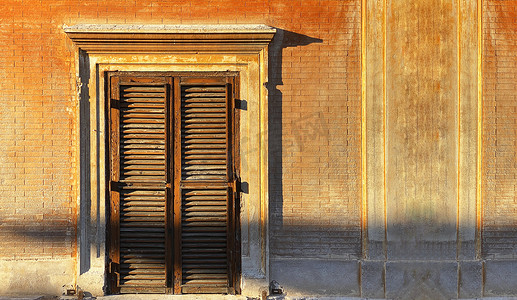 意大利日落时的阳光照亮了带有封闭木百叶窗的古老窗户。