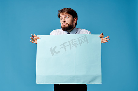 横幅广告摄影照片_情绪化的男士衬衫，打着领带，拿着横幅广告蓝色背景