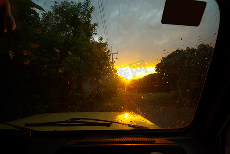 雨后玻璃摄影照片_泥路雨后和黄昏阳光下，从汽车透过湿挡风玻璃看去