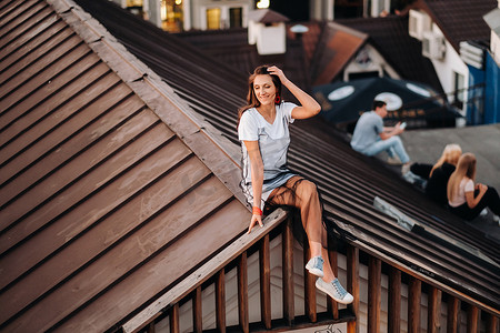 晚上，一个女孩坐在城市一所房子的屋顶上。